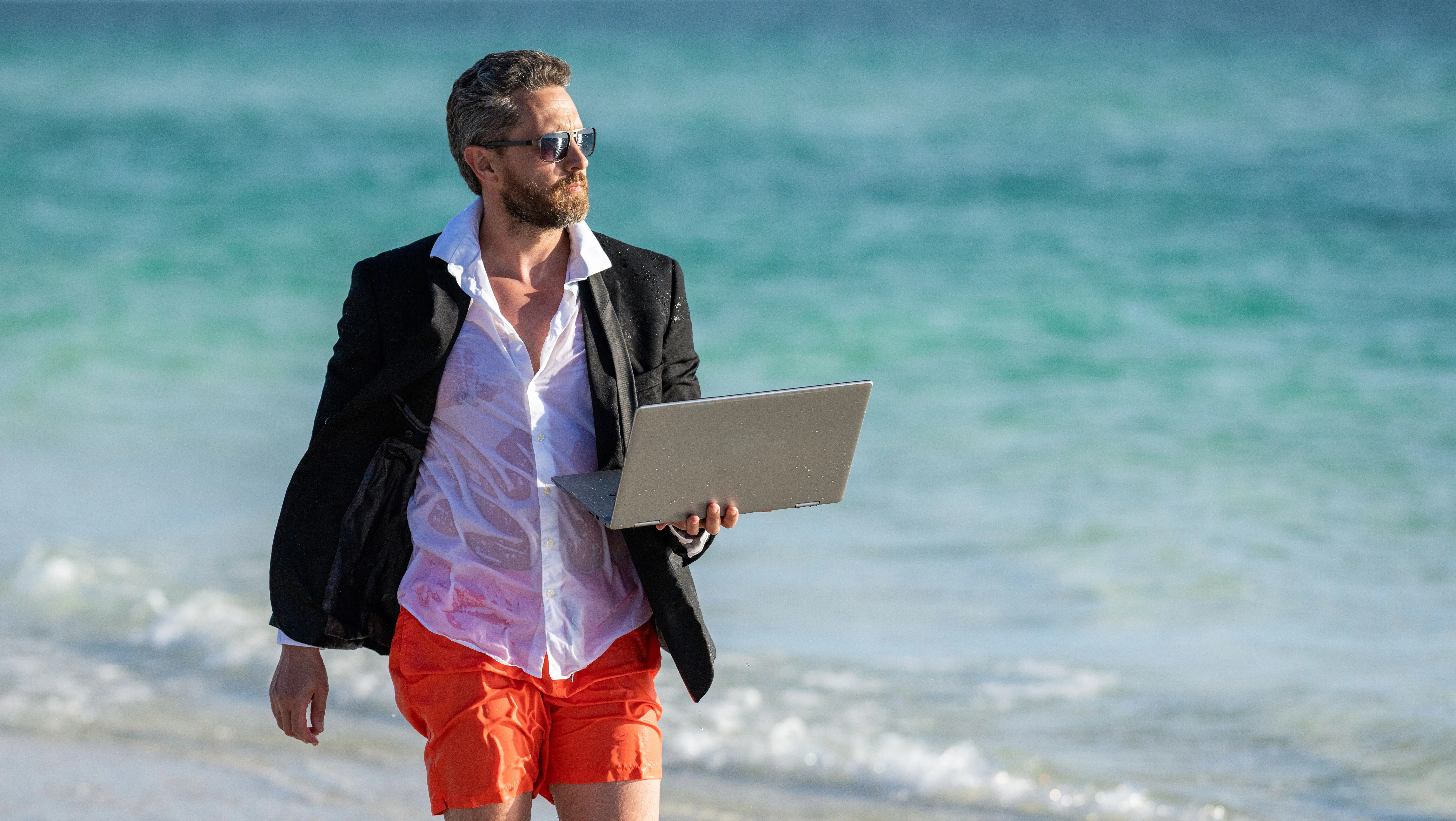 Remote-Arbeit im Sommer: Freelance-Konzept und Sommerreise – Geschäftsmann im Anzug im Sommerurlaub, der remote am Laptop arbeitet; freiberufliche Fernarbeit eines Geschäftsmanns, zweckgerichtete Reise.